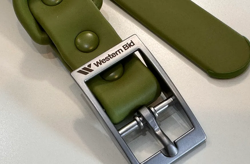 Close-up of an olive green silicone or rubber strap with a metal buckle engraved with the Western Bid logo